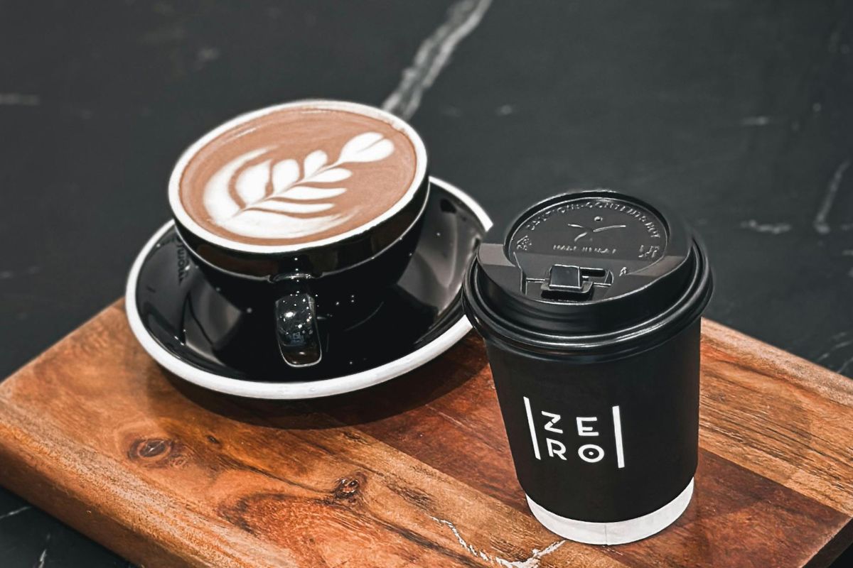 Filiżanka cappuccino z latte art obok czarnego kubka na wynos na drewnianej tacy.